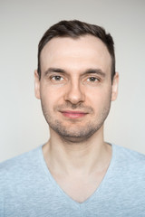Fototapeta premium Portrait of a young handsome fashionable guy with a bristle with a smile on his face in a gray shirt on a light background