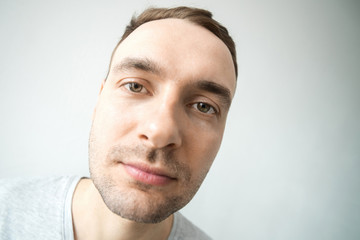 Portrait of a young handsome fashionable guy with a stubble and a smile on his face in a gray shirt on a light background. Wide angle, very large portrait
