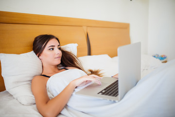 Smiling woman catching up on her social media as she relaxes in bed with a laptop computer on a lazy day