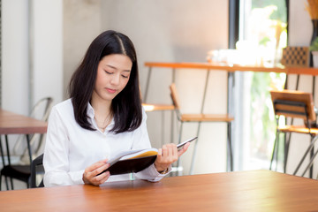 Beautiful business asian young woman reading on notebook on table, girl work at coffee shop, freelance businesswoman concept.