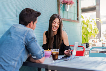 Happy young couple seating in a restaurant with a laptop