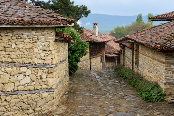 Fototapeta na wymiar Zheravna, Bulgaria - narrow cobbled road and rustic traditional houses made of stone and wood with bigroot cranesbill (Geranium macrorrhizum) along the stone wall