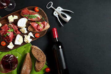 Wine bottle with cheese and traditional sausages on wooden board on black background with copy space