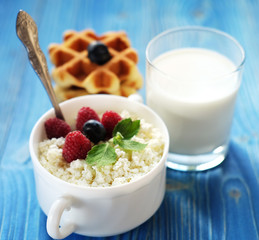 Time for breakfast. Cottage cheese with berries, waffles and milk on a wooden blue background.
