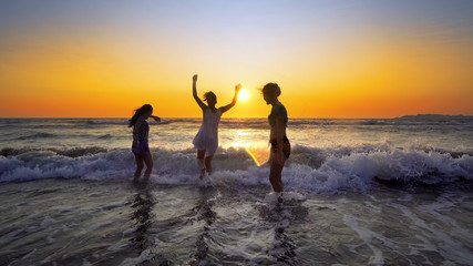 Group of female teens having fun jumping and splashing down the beach at sunset