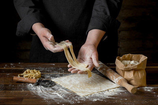 Men's chef  hands, close-up, holding sliced pastry for pasta over wooden table on brick wall background, home cooking concept.