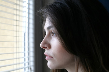 Woman portrait; young woman looking through the window; profile view.