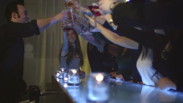 A bunch of people sitting at the bar and cheering with the bar tender
