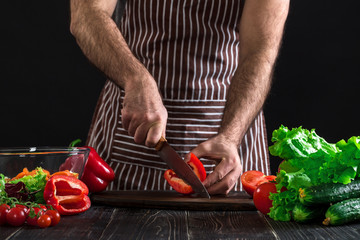 Man's hands cutting ripe pepper into slices on a table. On black background