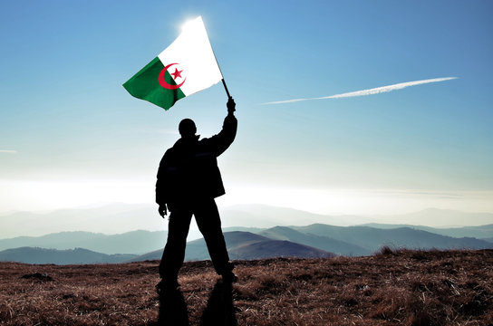 Successful silhouette man winner waving Algeria flag on top of the mountain peak