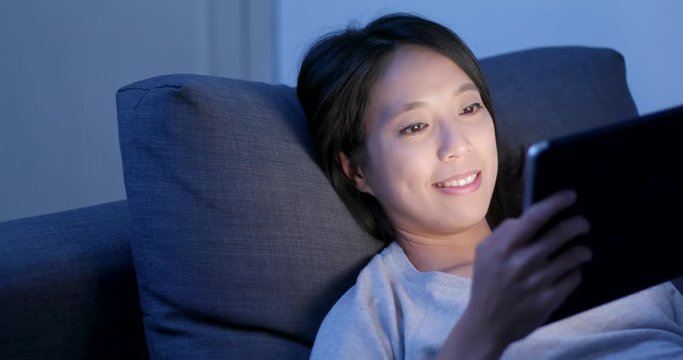 Woman watching on digital tablet computer and lying on sofa at night