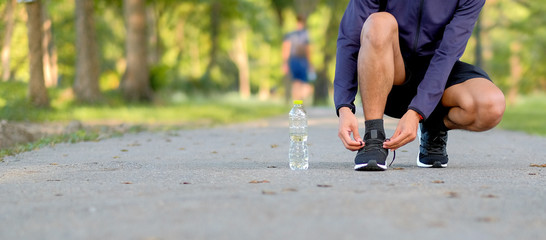 Young athlete man tying running shoes in the park outdoor, male runner ready for jogging on the...