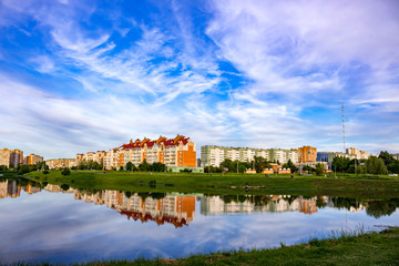 Fototapeta na wymiar Landscape of the pond on the background of the city on a summer day. Reflection of the sky and buildings in the water 