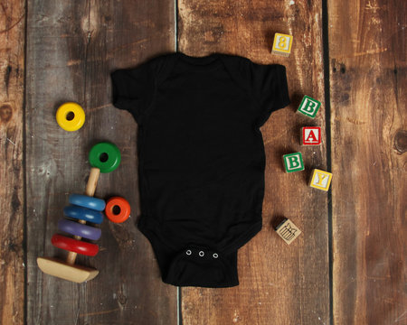 Mockup Flat Lay of black baby bodysuit shirt on rustic wood background with wooden blocks and baby toys