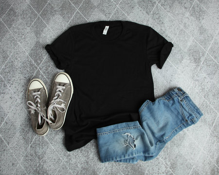 Mockup Flat Lay of Black T shirt with gray canvas shoes and ripped jeans on a gray background
