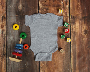 Mockup Flat Lay of gray baby bodysuit shirt on rustic wood background with wooden blocks and baby...