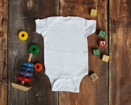 Mockup Flat Lay of white baby bodysuit shirt on rustic wood background with wooden blocks and baby toys