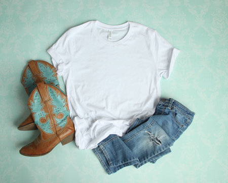 Mockup Flat Lay of White Tee shirt with cowboy boots and ripped jeans on an aqua blue background
