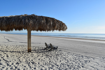 Tiki hut and chairs on a sandy tropical ocean beach vacation