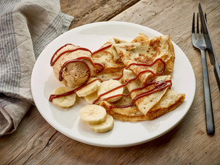 Crepes with banana and caramel icecream on wooden desk