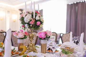 White candles on metal gold chandelier stand on tables at luxury wedding reception in restaurant. stylish decor and adorning