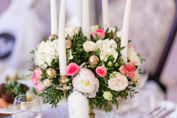 White candles on metal gold chandelier stand on tables at luxury wedding reception in restaurant. stylish decor and adorning