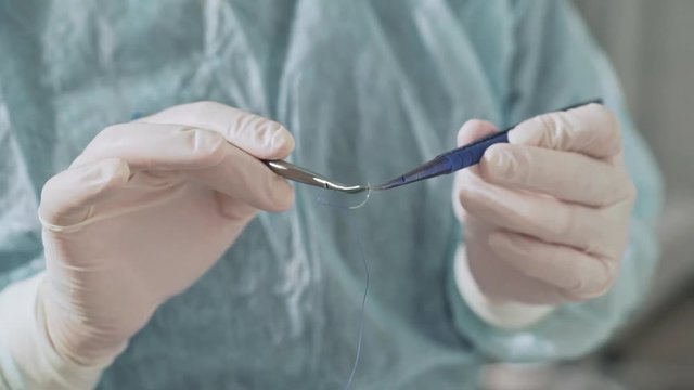 Closeup, the surgeon holds a clamp with a surgical needle in his hand. Sterile medical instruments in the hospital. Preparation of medical equipment before the operation. The concept of health