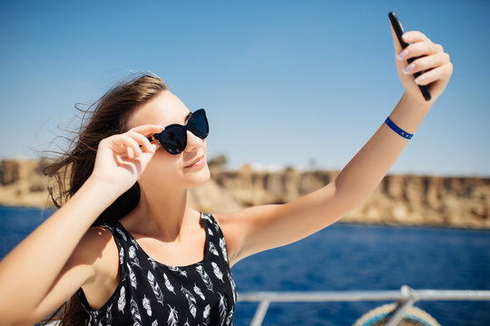 Young beautiful brunette girl making selfie using phone while relaxing on the luxury yacht