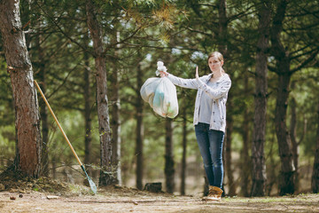Fototapeta premium Young woman cleaning rubbish holding trash bags and showing stop gesture with palm in park on green background. Problem of environmental pollution. Stop nature garbage, environment protection concept.
