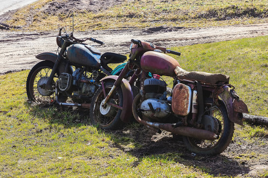 two old motorcycles are parked in green meadow