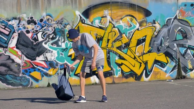 Graffiti painter is putting his colouring barrels into the backpack and walking away