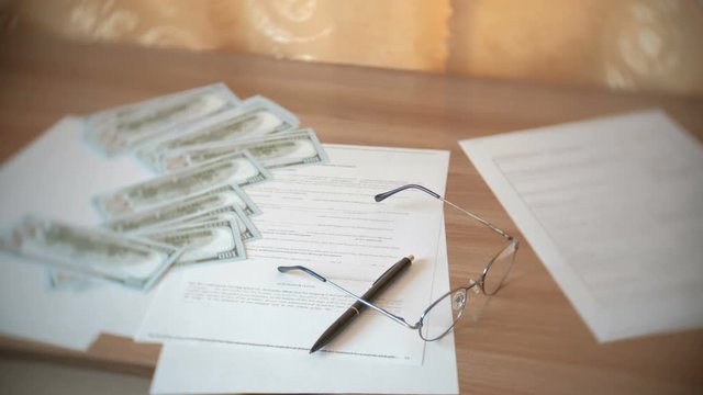 Glasses, papers, money, documents and a pen on the table.