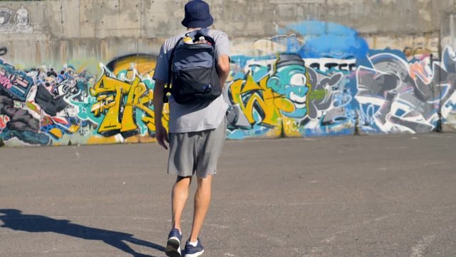 Graffiti artist is lifting his backpack with paint canisters and going towards the graffiti wall