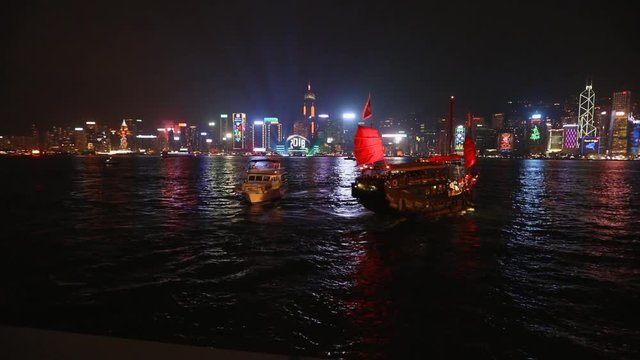 Hong Kong night scene - Central island illuminated by city lights; shot from Star Ferry pier at Kowloon; tour boats loaded with tourists in foreground; handheld footage;