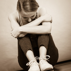 Sad depressed young teenage girl sitting by wall