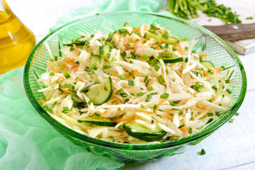 Dietary salad with cabbage, cucumber, carrot, greens. Juicy spring salad from fresh vegetables on a white wooden background. Proper nutrition.