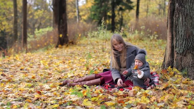 woman with baby sitting in autumn park