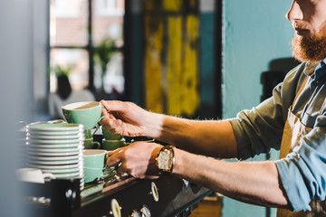 cropped image of young male barista in apron taking mugs in coffee shop