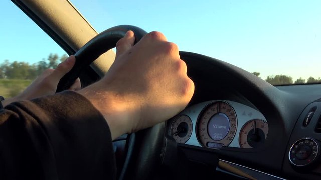 4K. Driving at sunset on a highway. Close up of hand on steering wheel of the car. Holds the steering wheel of the car with both hands-Adrian.