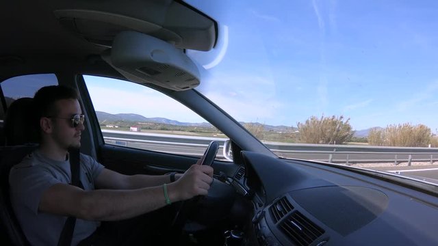 4K. A young European man is driving a car on a highway. It takes both hands to the steering wheel and is concentrated in the conduction. Car interior. The day is sunny-Adrian.