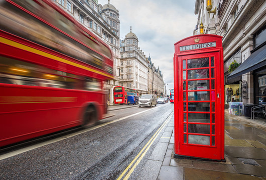 London, England - Iconic blurred vintage red double-decker bus on the move with traditional red telephone box in the center of London at daytime