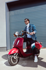 stylish young man in denim jacket on vintage red scooter