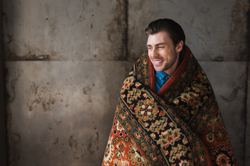 happy young man covered in rug in front of concrete wall