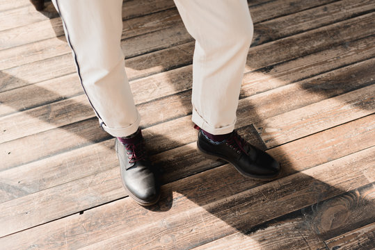cropped shot of man in stylish shoes and pants standing on rustic wooden floor