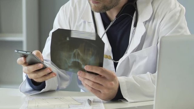 Doctor looking at nasal bones x-ray and talking with patient on cellphone