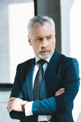 portrait of confident senior businessman standing with crossed arms and looking away