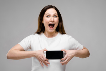Fototapeta premium Emotional smiling happy plus size model standing in studio looking in camera offering mobile phone to a client