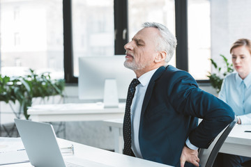 side view of senior businessman suffering from pain in back while sitting at workplace