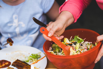 a woman's hand mixes a salad with a plastic spoon