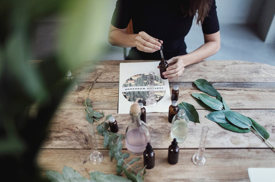Midsection of female owner using pipette for mixing liquid from bottle while sitting at table in perfume workshop